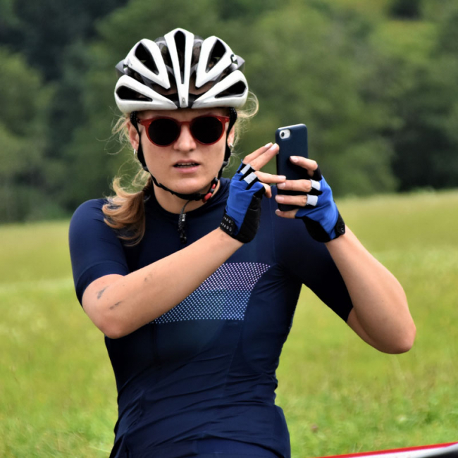 Female Cyclist wearing Round Sunglasses and holding a phone- Beginners guide to cycling sunglasses